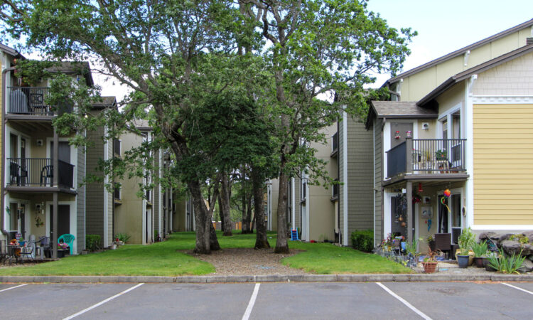 Lakewood Village Apartments - Courtyard 1 A courtyard at a three-story apartment building with tall trees.